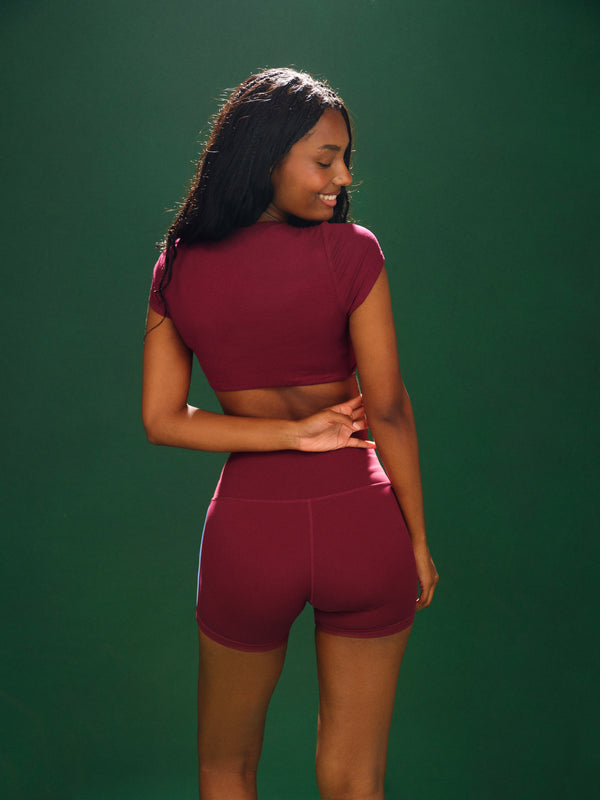 Woman wearing a maroon athletic outfit against a green background