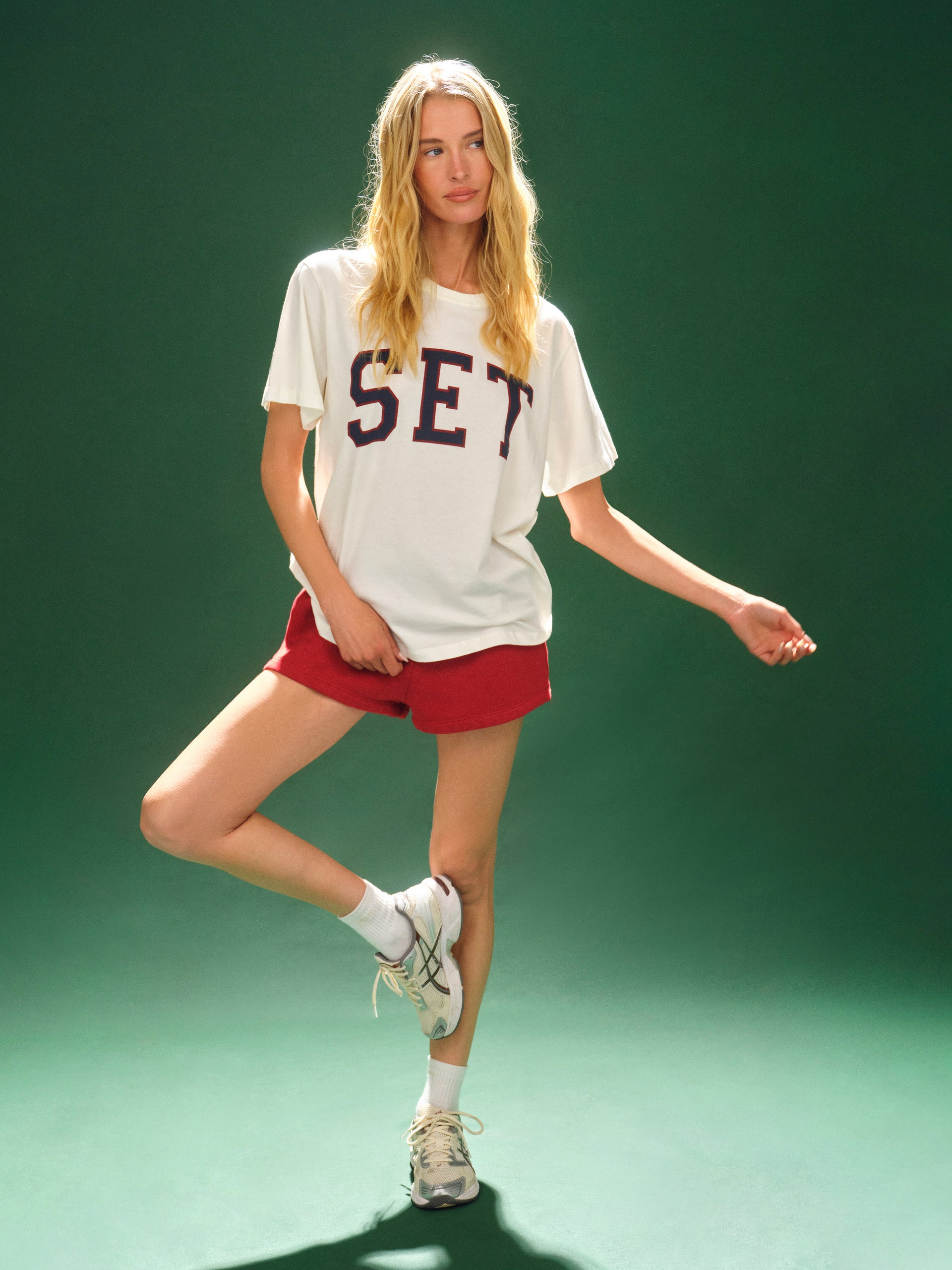 Woman wearing a white t-shirt with 'SET' and red shorts on a green background