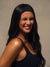 A woman with long dark hair wearing a black athletic headband and a black sports tank top, smiling and squinting against a neutral beige background.