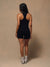 A woman is shown from behind wearing a black athletic tank top and matching black shorts, standing against a plain beige studio backdrop.