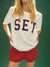 Person wearing a white t-shirt with 'SET' printed on it against a green background