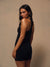 A woman wearing a black sleeveless athletic romper or bodysuit with matching shorts, photographed against a plain warm beige studio background.