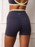 Rear view of a person wearing high-waisted navy athletic shorts with a cream waistband and a small white 'SET' logo, paired with a matching sports bra in a light interior setting.
