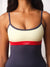 A close-up of a woman wearing a color-blocked athletic tank top with a cream upper section, a red waistband, and a dark navy lower section and straps.