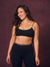 A woman modeling a matching black activewear set with leopard print trim, consisting of a sports bra and high-waisted leggings, against a textured dark purple studio backdrop. <model-info> Christina wears a size L and is 5’9, 29½” waist, 36" bust.</model-info> 