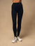 A model from the waist down wearing black high-waisted leggings and white trail running shoes, standing against a solid beige studio background.