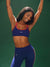 Woman wearing a blue sports bra and leggings with a green background <model-info>Umi wears a size XS and is 5’8½”, 23½” waist, 32B bust.</model-info>