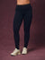 A person wearing black high-waisted leggings with a leopard-print waistband, paired with off-white sneakers, standing against a textured dark mauve studio backdrop.