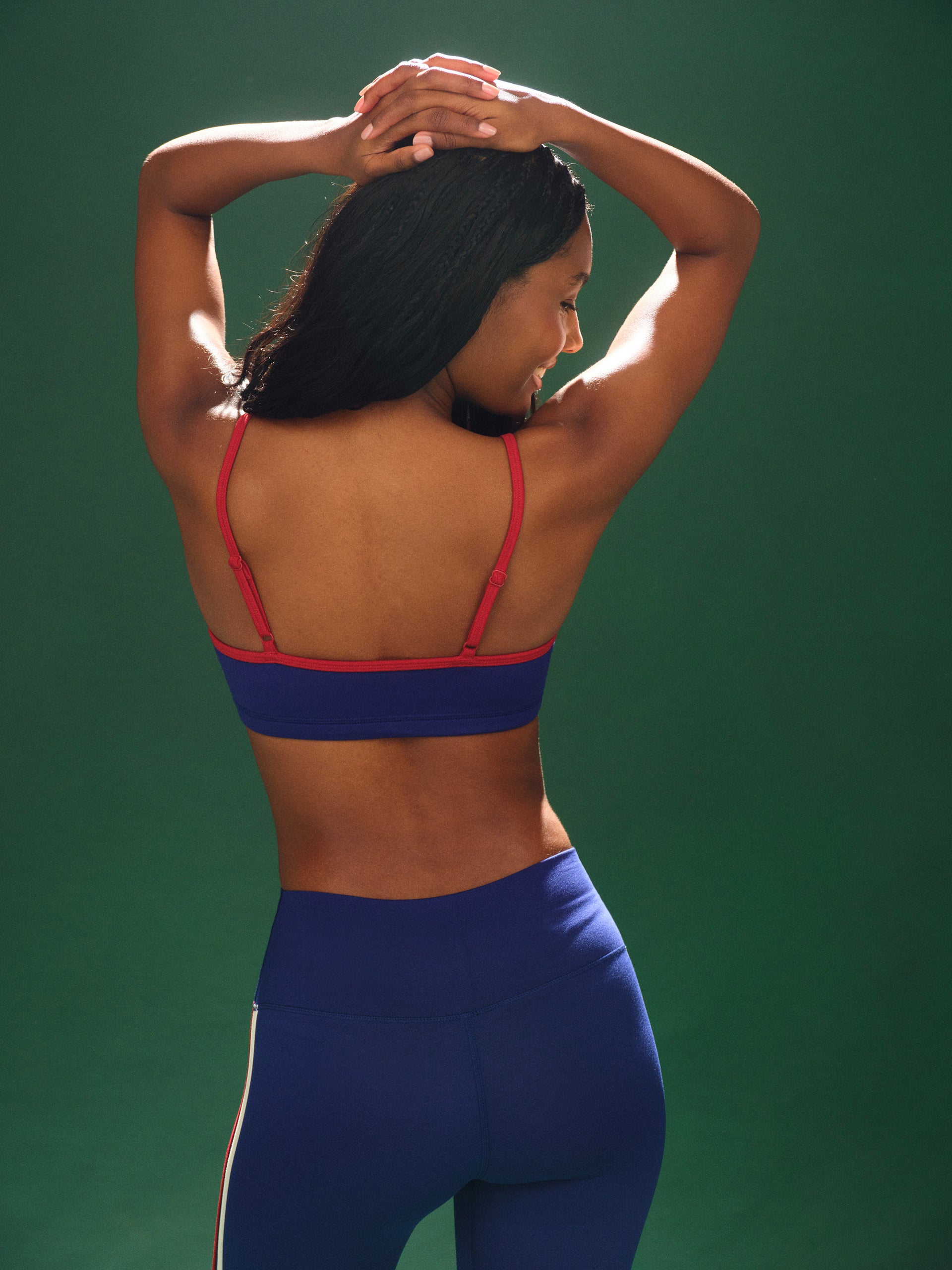 Woman wearing a blue sports bra and leggings with red straps against a green background