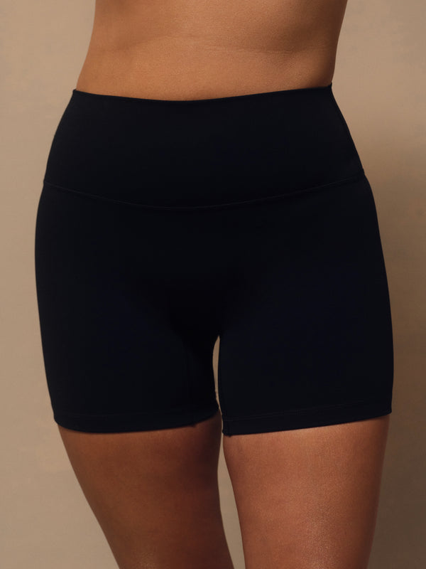 Black high-waisted athletic biker shorts worn by a model, shown from the waist to mid-thigh against a plain beige studio background. 