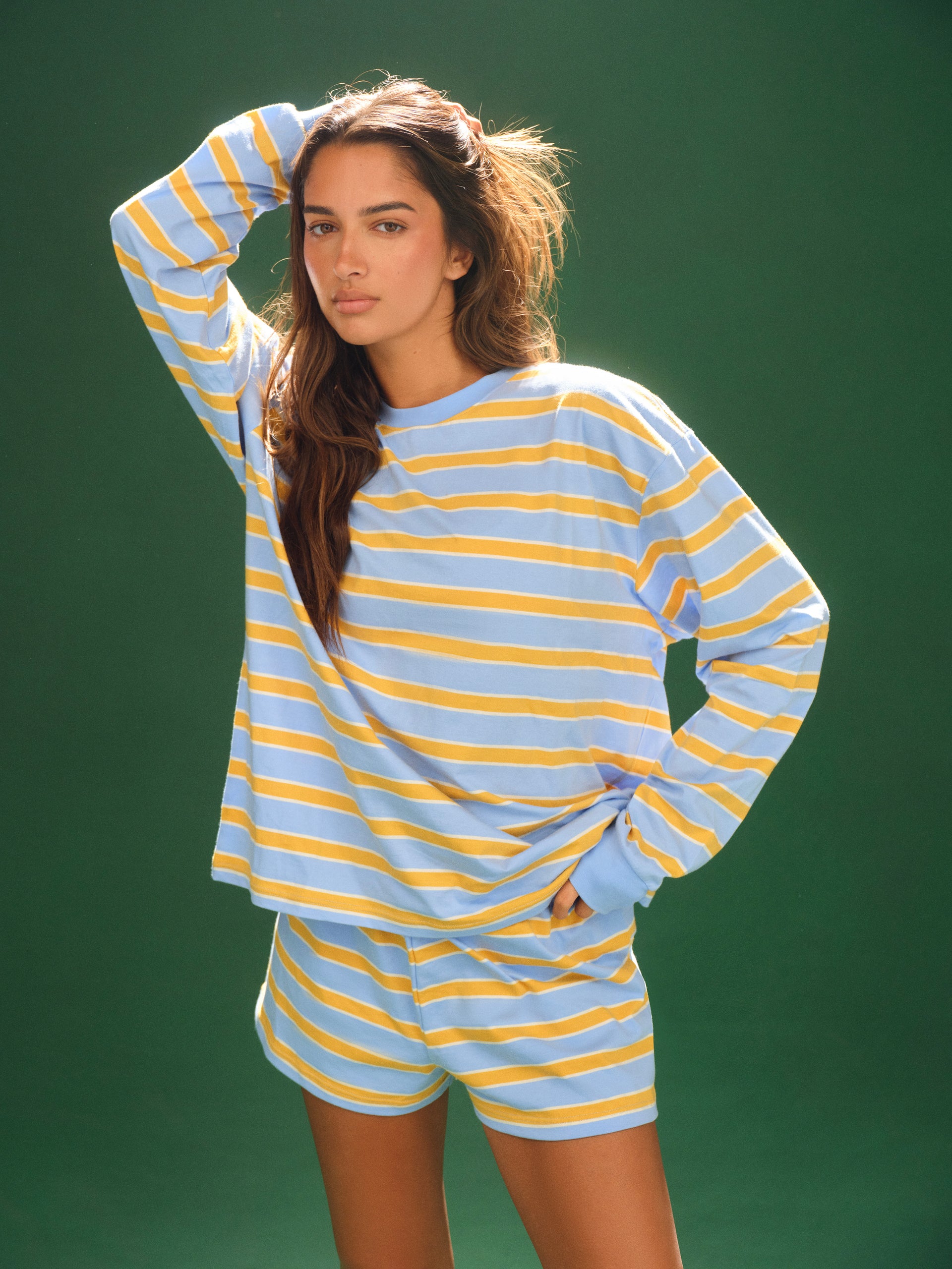 Woman wearing a blue and yellow striped pajama set against a green background <model-info>Kushi wears a size XS and is 5'8, 24” waist, 32C bust.</model-info>