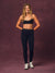 A woman modeling a black athletic set consisting of a sports bra and high-waisted leggings with leopard print trim, standing against a textured dark purple studio backdrop. <model-info> Andrea wears a size S and is 5’9”, 25½” waist, 32” bust.</model-info>