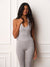 A woman modeling a light gray athletic set consisting of a halter-style tank top and matching leggings, standing against a white paneled wall. <model-info>Meeya wears a size XS and is 5’8”, 23” waist, 32B bust.</model-info>