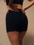 Rear view of a woman wearing black high-waisted athletic shorts with a small white 'SET' logo near the hem, against a plain beige studio background.