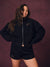 A woman modeling a black zip-up jacket and matching black shorts with gold 'SET' embroidery, posed against a textured dark burgundy backdrop. <model-info> Christina wears a size L and is 5’9, 29½” waist, 36" bust.</model-info> 