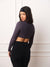 A woman wearing a dark grey long-sleeve crop top and black leggings, shown from the back against a white paneled wall.