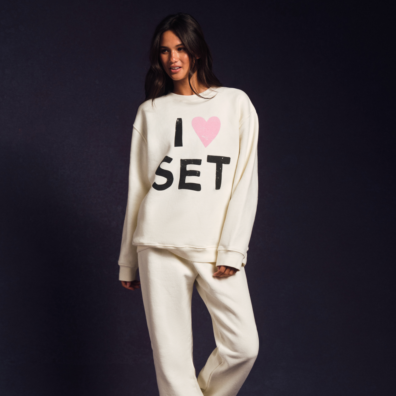 Woman wearing a white sweatshirt with 'I ❤️ SET' text on a dark background