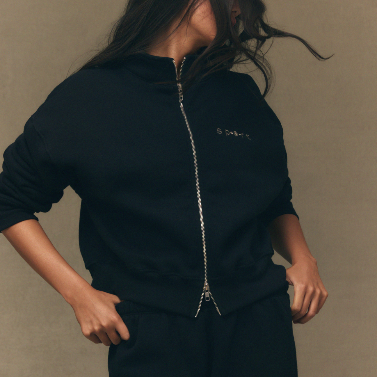 Person wearing a black tracksuit with a brand logo on a beige background