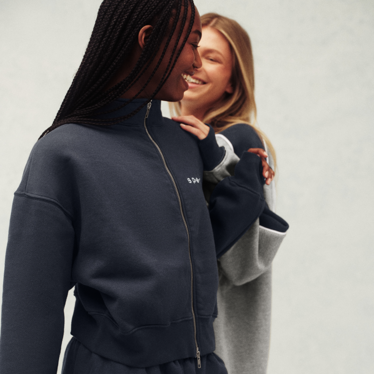 Two people wearing navy tracksuits with a brand logo on a light gray background