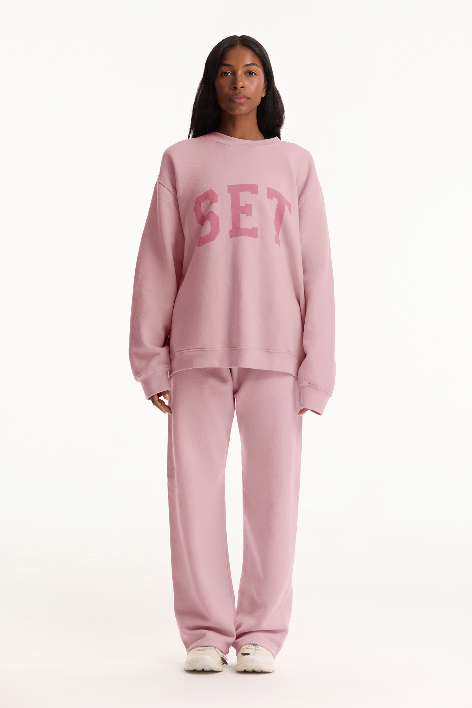 Person wearing a pink 'SET' sweatshirt and pants on a white background
