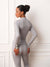 A woman wearing a light gray long-sleeve mock neck athletic top and matching leggings, shown from the back in a bright indoor setting with white paneled walls.