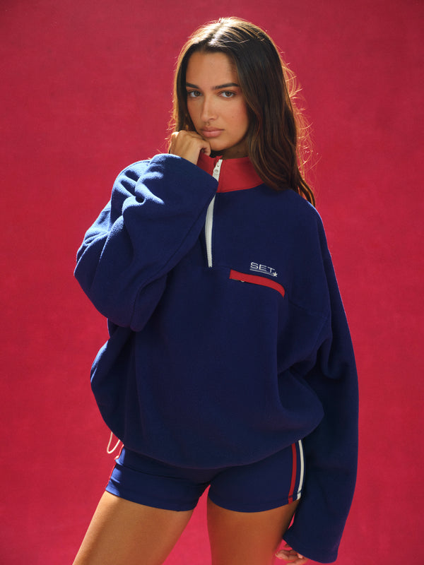 Woman wearing a blue tracksuit with red accents against a red background 
