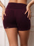 A close-up back view of a model wearing high-waisted athletic shorts in a deep burgundy color. The brand name 'SET' is printed in white on the left hem. <model-info>Leah wears a size M and is 5’7”, 25” waist, 32D bust.</model-info>