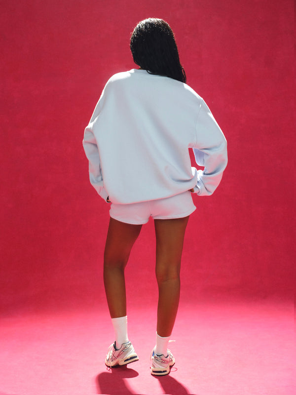 Person wearing a light blue sweatshirt and shorts on a red background