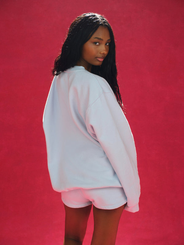 Person wearing a light blue sweatshirt and shorts on a red background