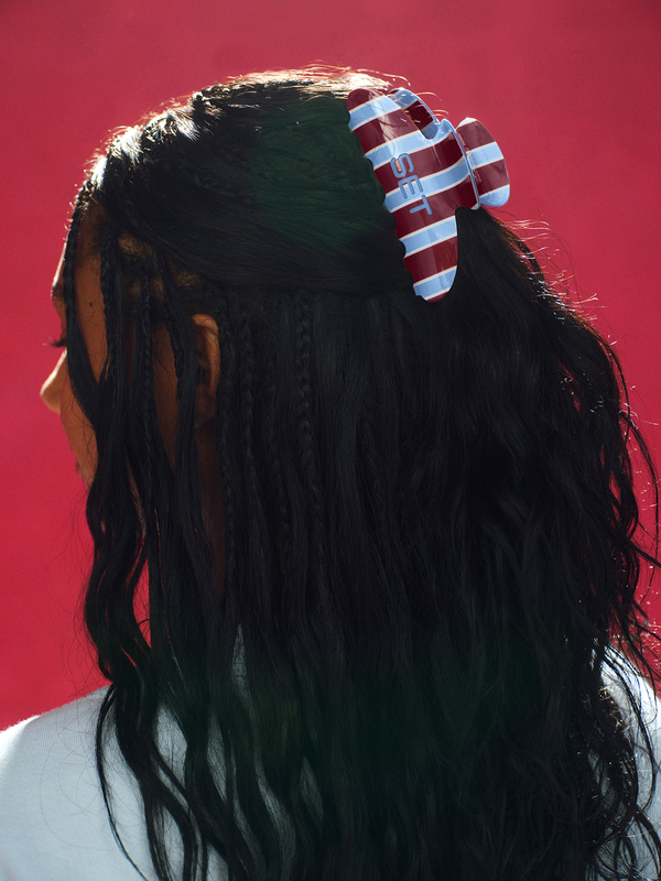 Person with braided hair wearing a red and white striped headband against a red background