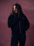 A woman wearing a dark navy zip-up hoodie with 'SET' embroidered on the chest and matching dark pants, posing against a textured mauve-pink studio backdrop. <model-info> Christina wears a size L and is 5’9, 29½” waist, 36" bust.</model-info> 