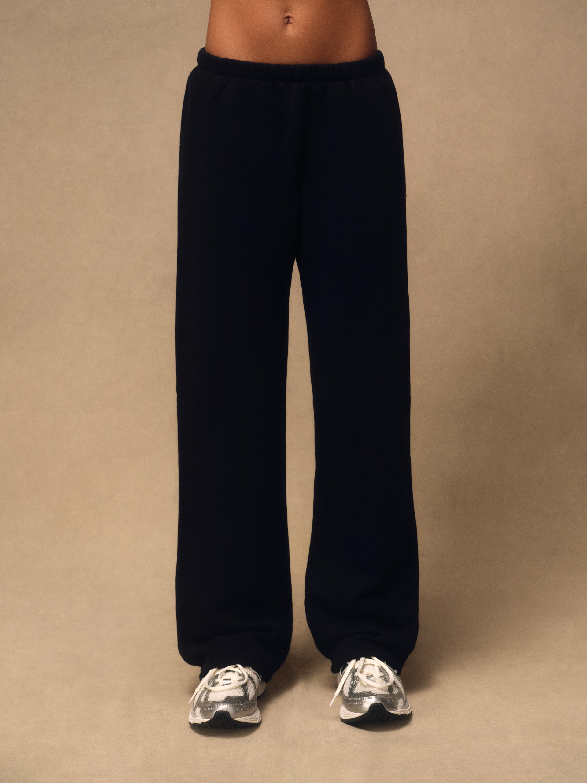 Black wide-leg sweatpants worn by a model, shown from the waist down against a plain beige studio background.