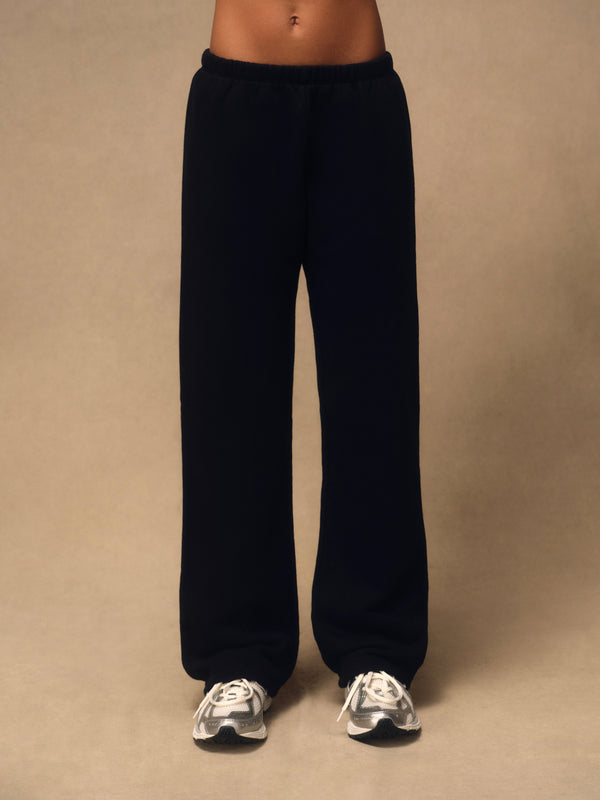 Black wide-leg sweatpants worn by a model, shown from the waist down against a plain beige studio background.