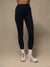 A person from the waist down wearing high-waisted black leggings, white socks, and white trail running shoes against a neutral beige studio background.