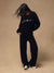 A model wearing a black sweatshirt and matching sweatpants set, featuring the word 'sport' printed in white across the chest, posed against a solid beige studio backdrop.