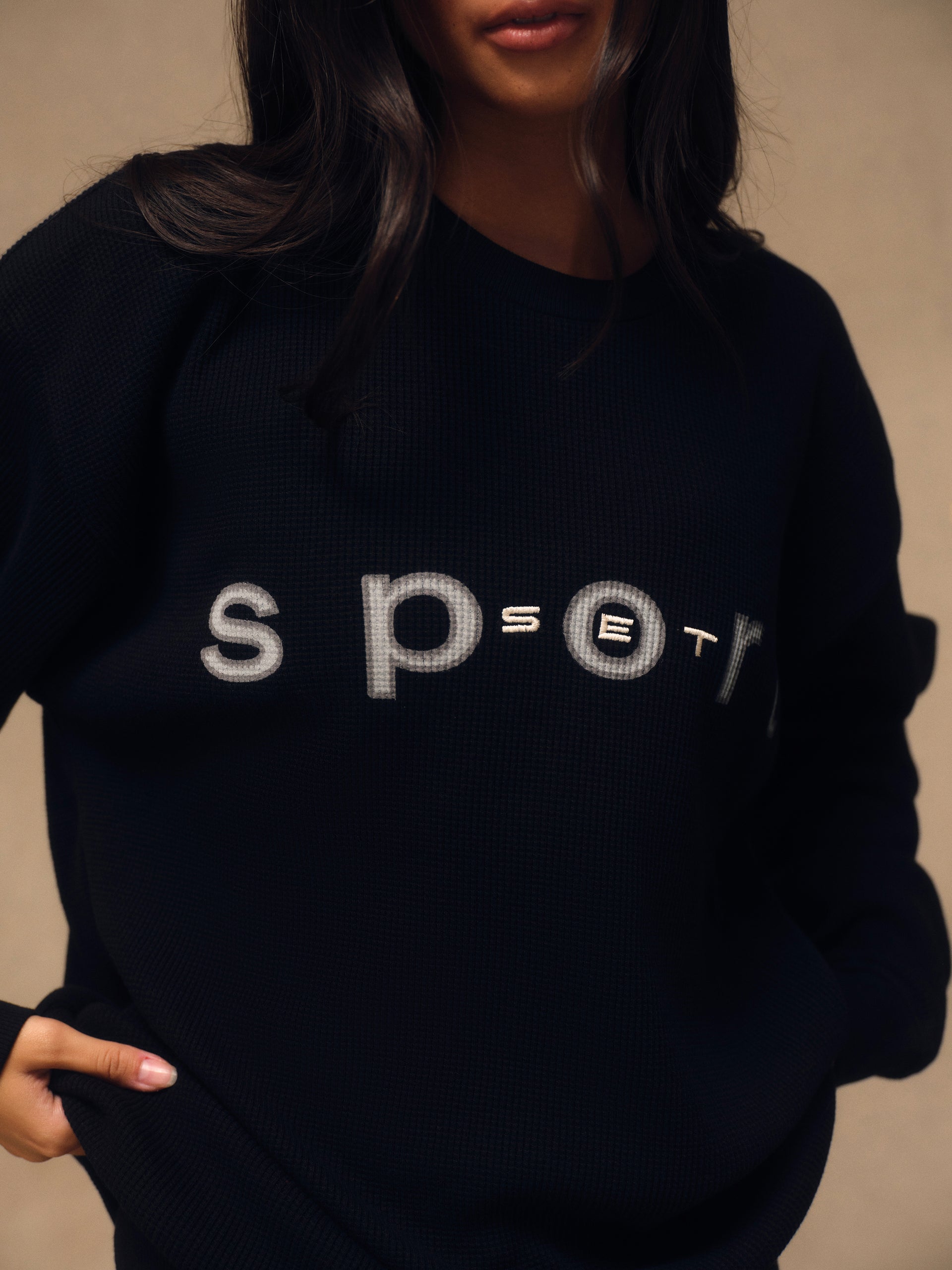 A close-up of a person wearing a black knit sweater with the word 'sport' printed across the chest in a textured light gray font.