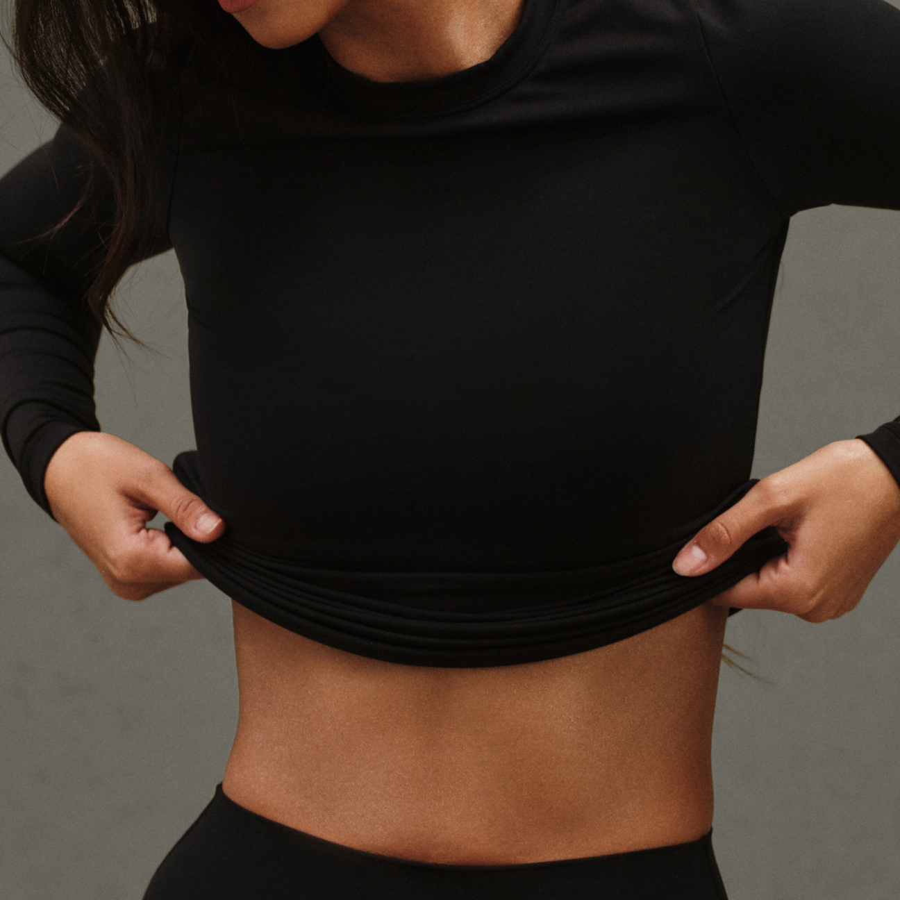Person wearing a black long-sleeve top against a gray background