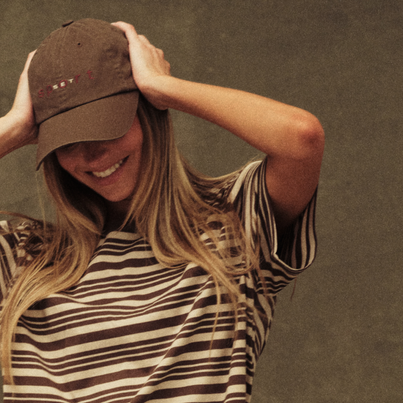 Woman wearing a brown cap and striped shirt against a plain background
