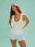 Woman wearing a white tank top and light blue shorts against a light green background <model-info>Kushi wears a size S and is 5'8, 24” waist, 32C bust.</model-info>