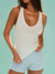 Woman wearing a white tank top and light blue shorts against a teal background