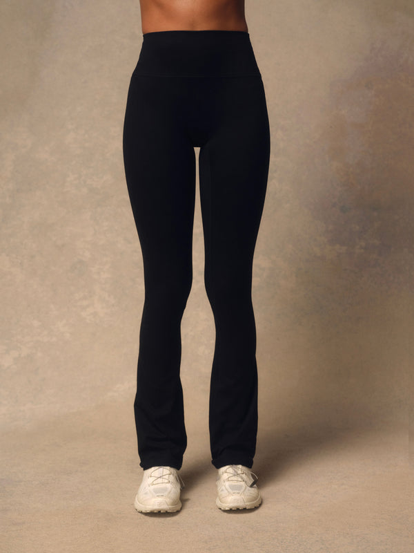 Black high-waisted leggings worn by a model, shown from the waist down against a textured beige studio backdrop.
