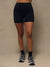 A person wearing dark navy high-waisted biker shorts, black socks, and gray running shoes, standing against a plain beige studio backdrop.