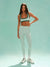 Woman wearing a green sports bra and light gray leggings on a light blue background