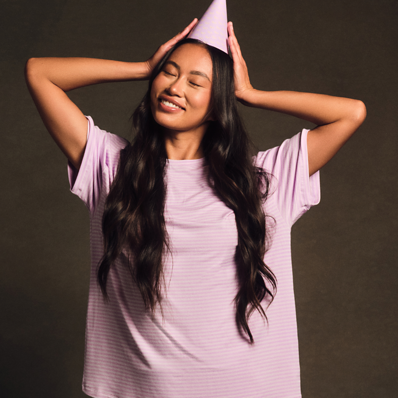 Woman wearing a purple dress and party hat with a dark background
