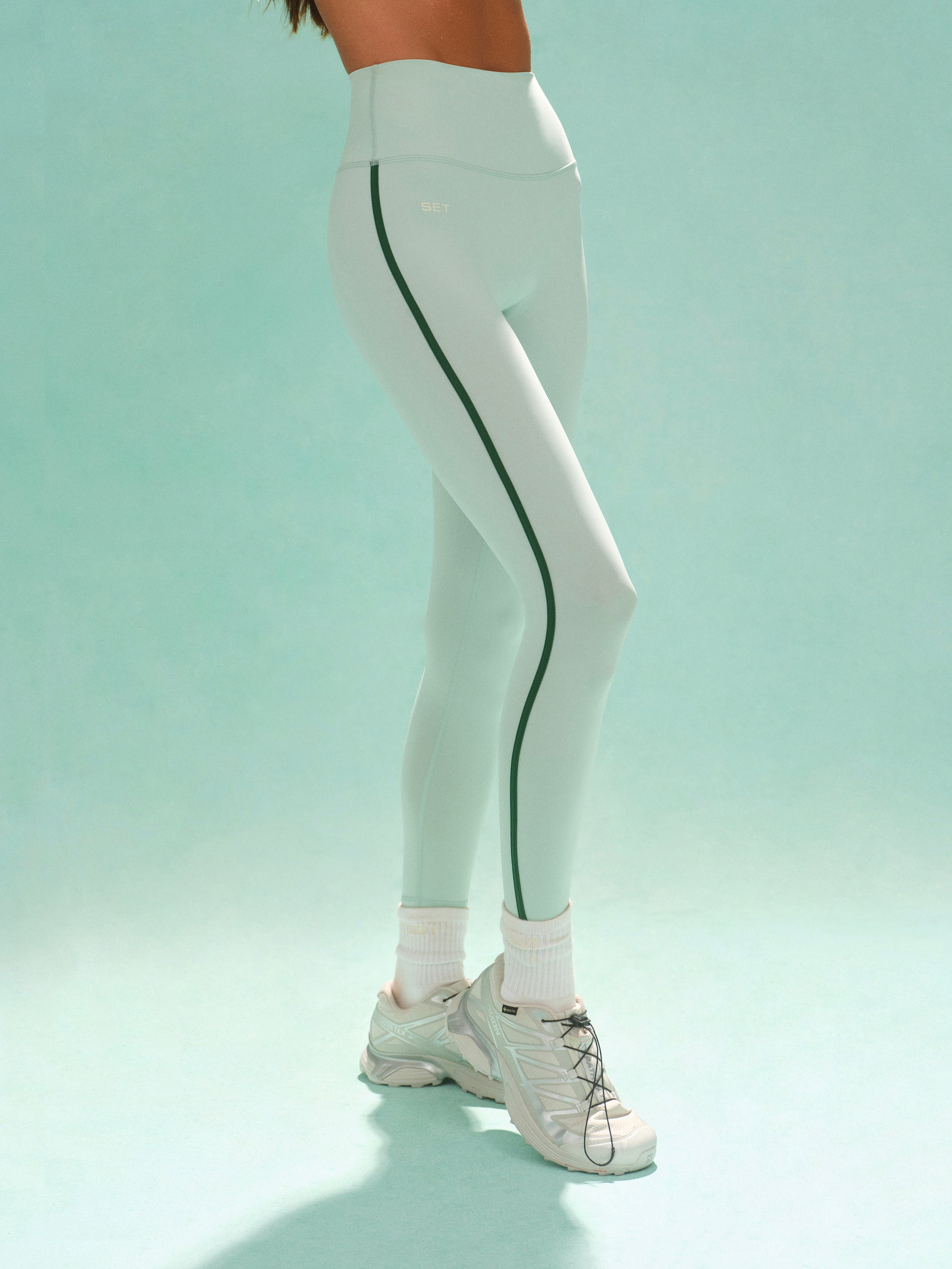 White leggings with green stripes worn by a person on a light blue background