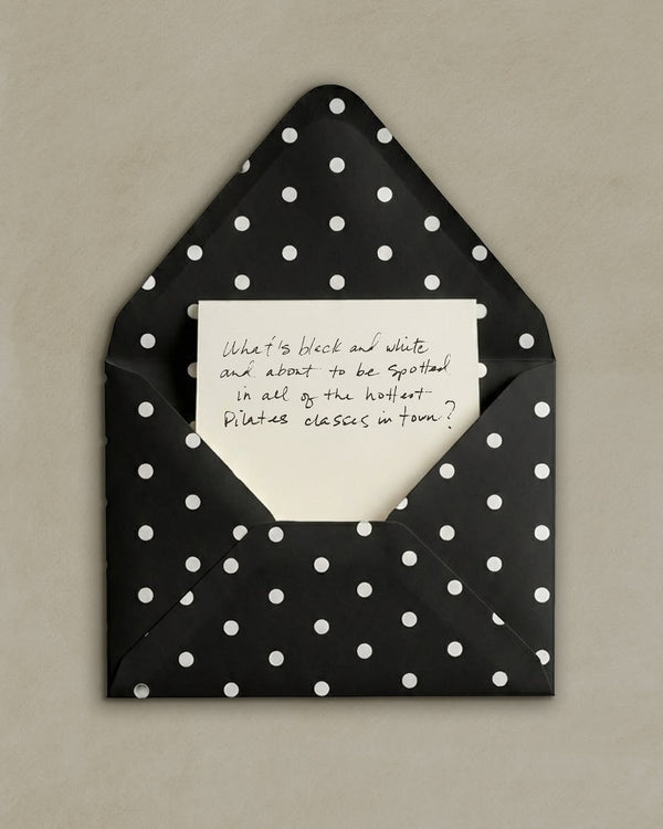 Black polka dot envelope with a white card inside on a beige background