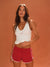 Woman wearing a white tank top and red shorts against an orange background <model-info>Jocelyn wears a size S and is 5'9, 23” waist, 32B bust.</model-info>