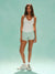 Woman wearing a white tank top and light green shorts on a light blue background