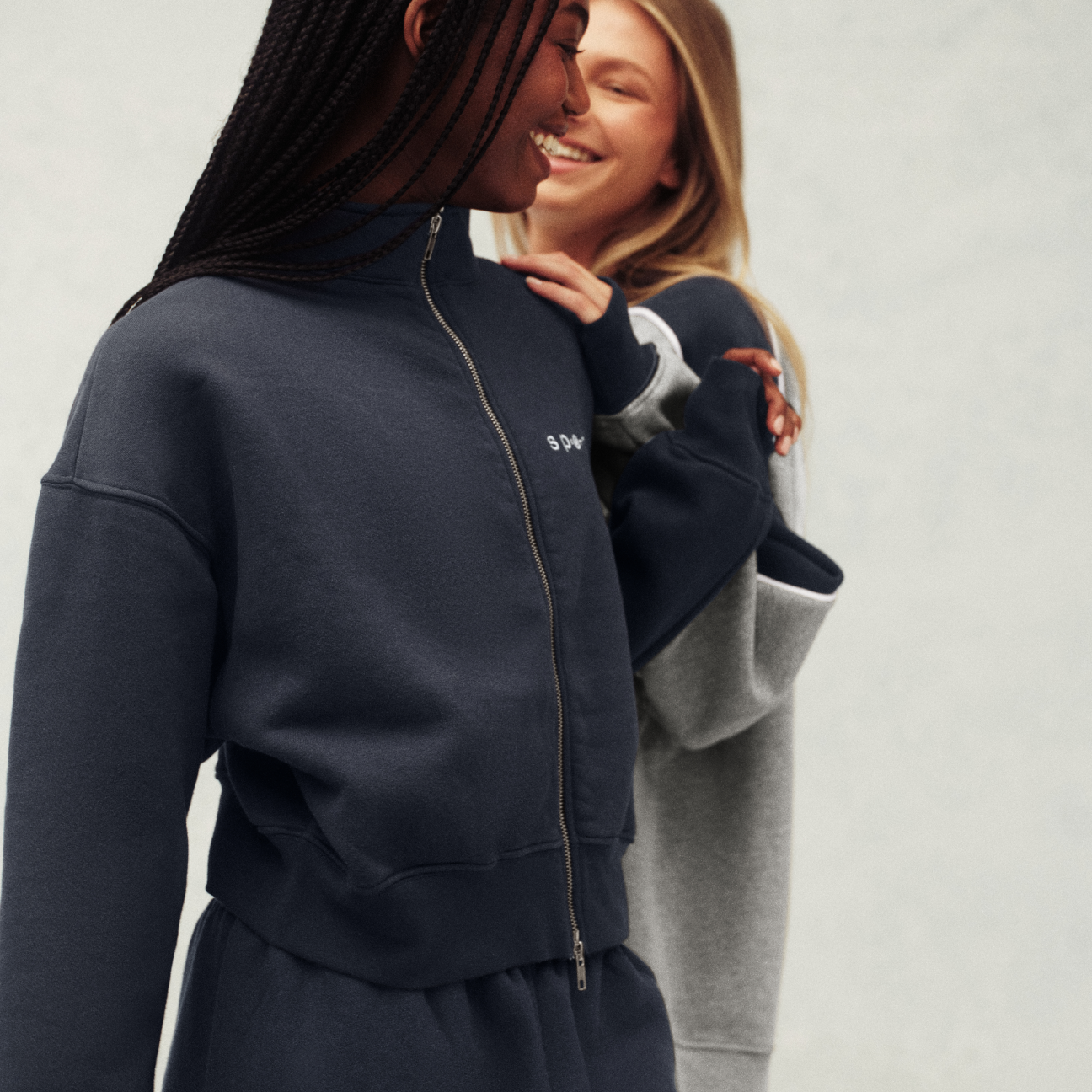 Two people wearing navy and gray tracksuits with a visible brand logo on a light background.