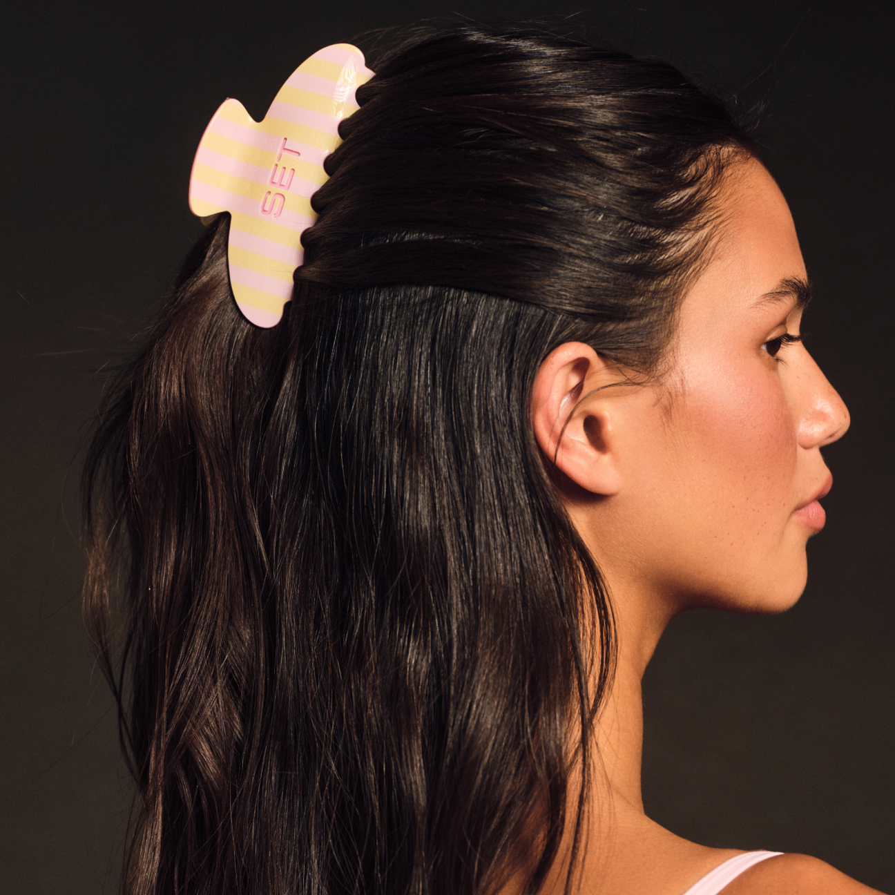 Woman with a pink and yellow hair clip in her hair against a dark background